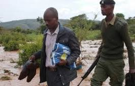 A pricipal crosses an over flowing river after a heavy down pour carrying exam papers (Photo Courtesy)