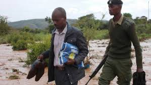 A pricipal crosses an over flowing river after a heavy down pour carrying exam papers (Photo Courtesy)